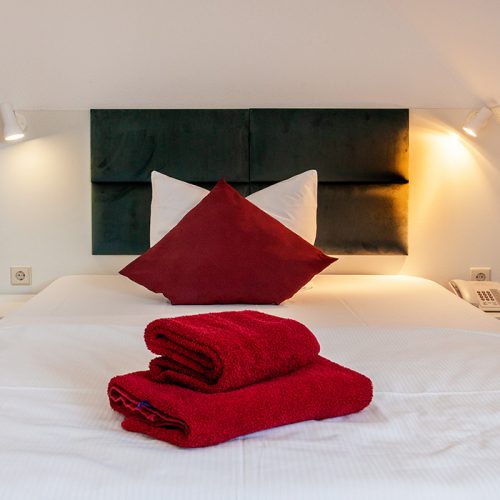 Einzelbett mit rotem Kissen und roten Handtüchern