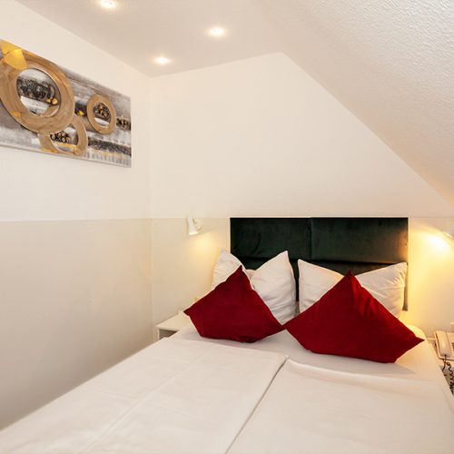 Doppelbett mit roten Kissen und Bild an der Wand